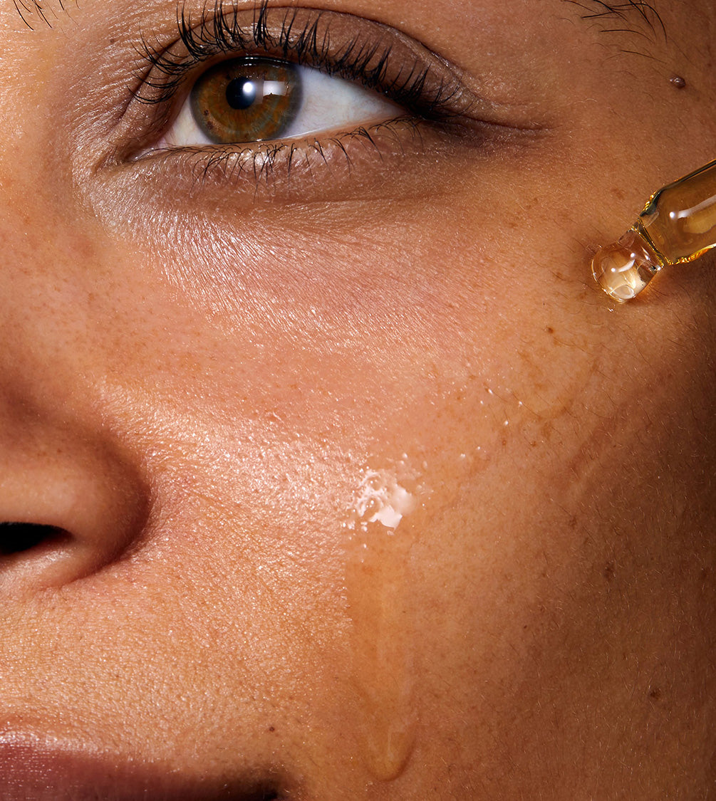 Model applying Miracle Facial Oil to her face with a pipette. The skin where the product has been applied look glowy and hydrated.