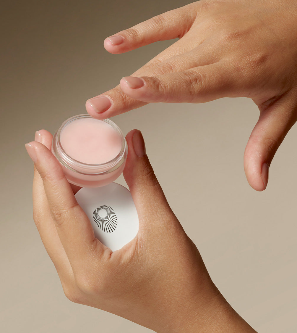 Hands are holding a jar of Perfecting Lip Balm.