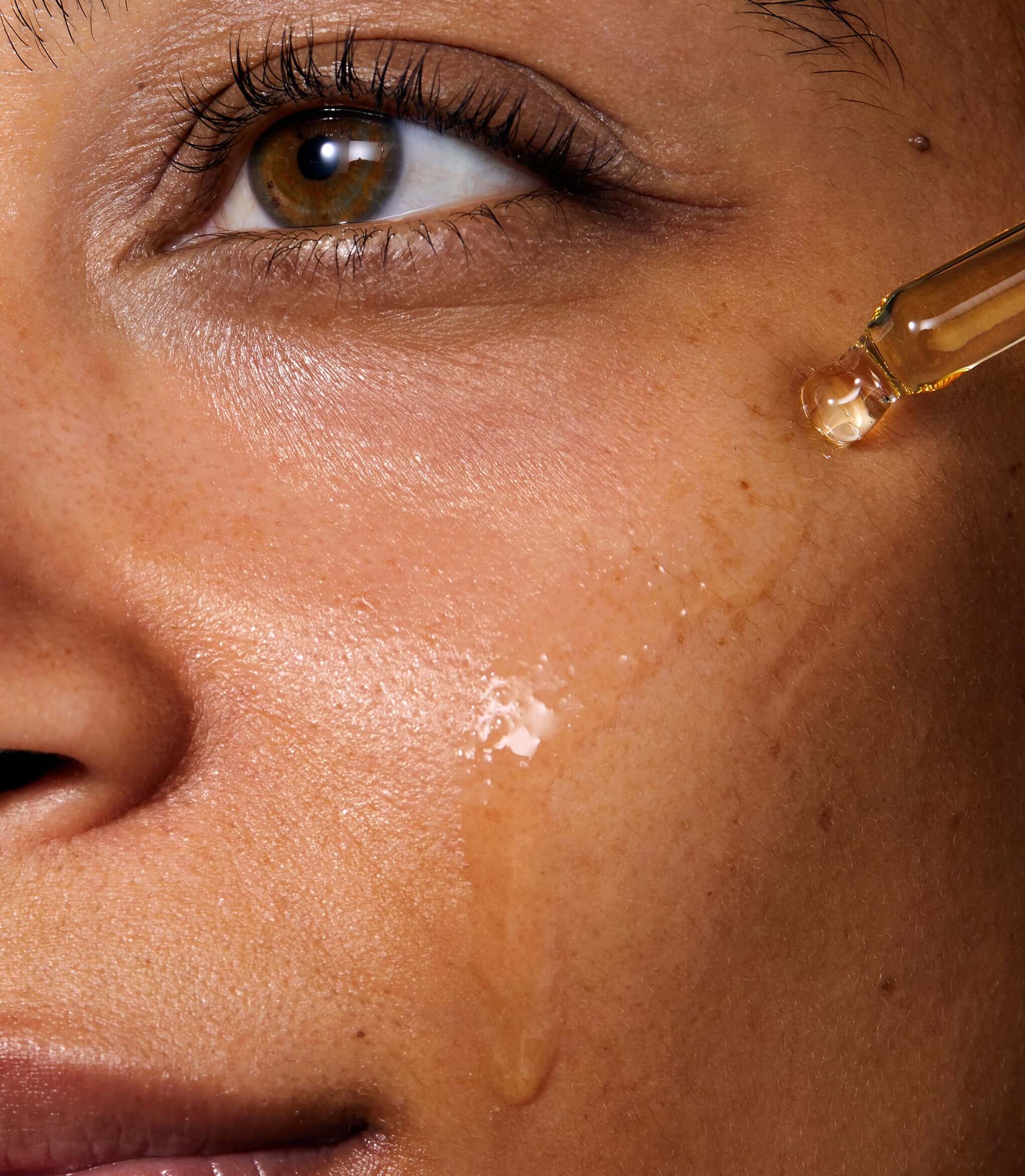 Model applying Miracle Facial Oil to her face with a pipette. The skin where the product has been applied look glowy and hydrated.