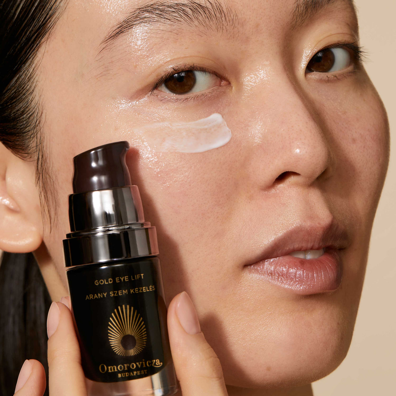 A close up of models face holding Gold Eye Lift Next to her eyes. A swatch of product is applied under her eye.