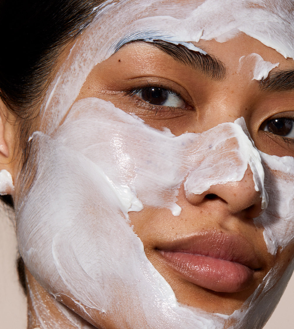 A close up of model's face with Queen cleanser applied over her face. the product is white and creamy applied in a thick layer.