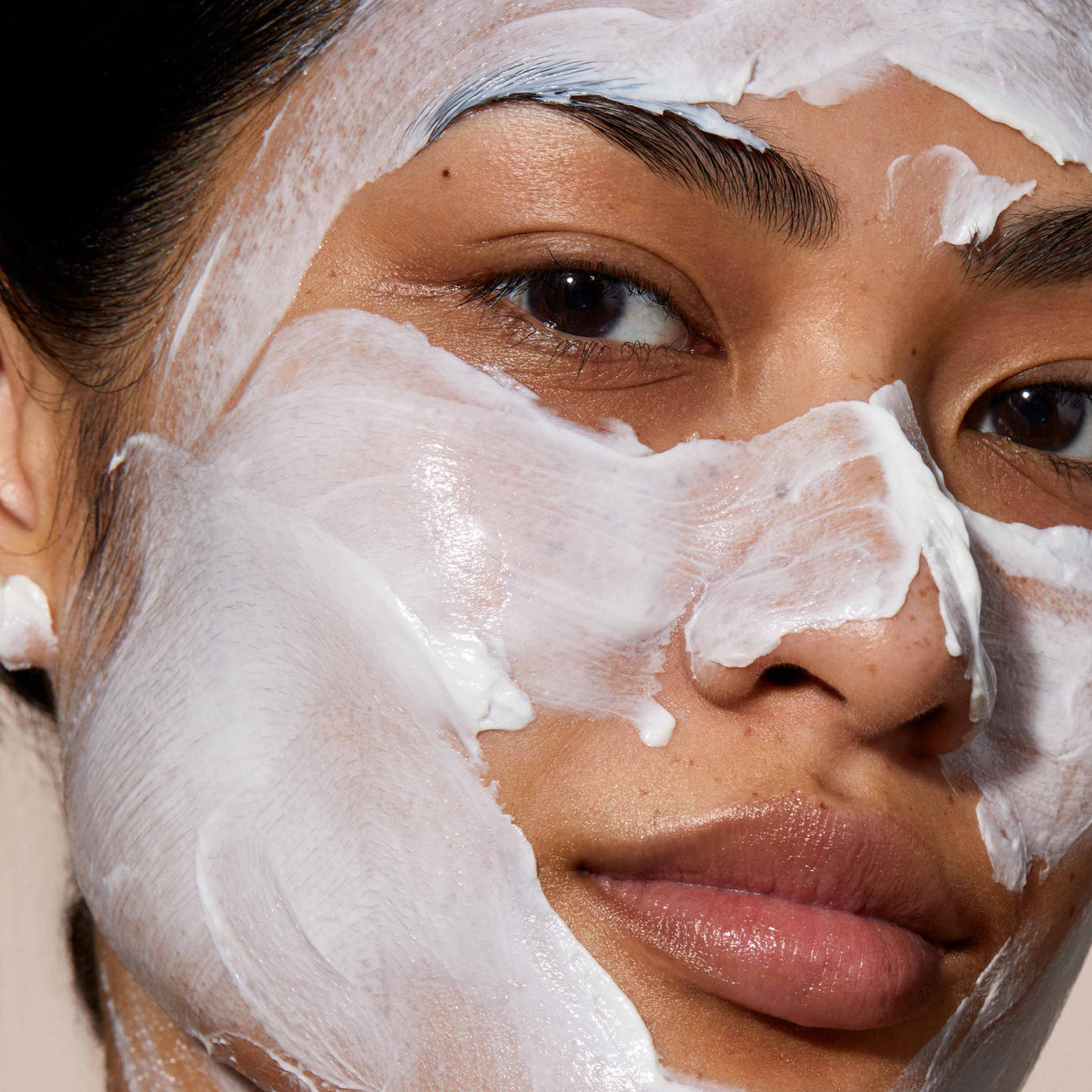 A close up of model's face with Queen cleanser applied over her face. the product is white and creamy applied in a thick layer.