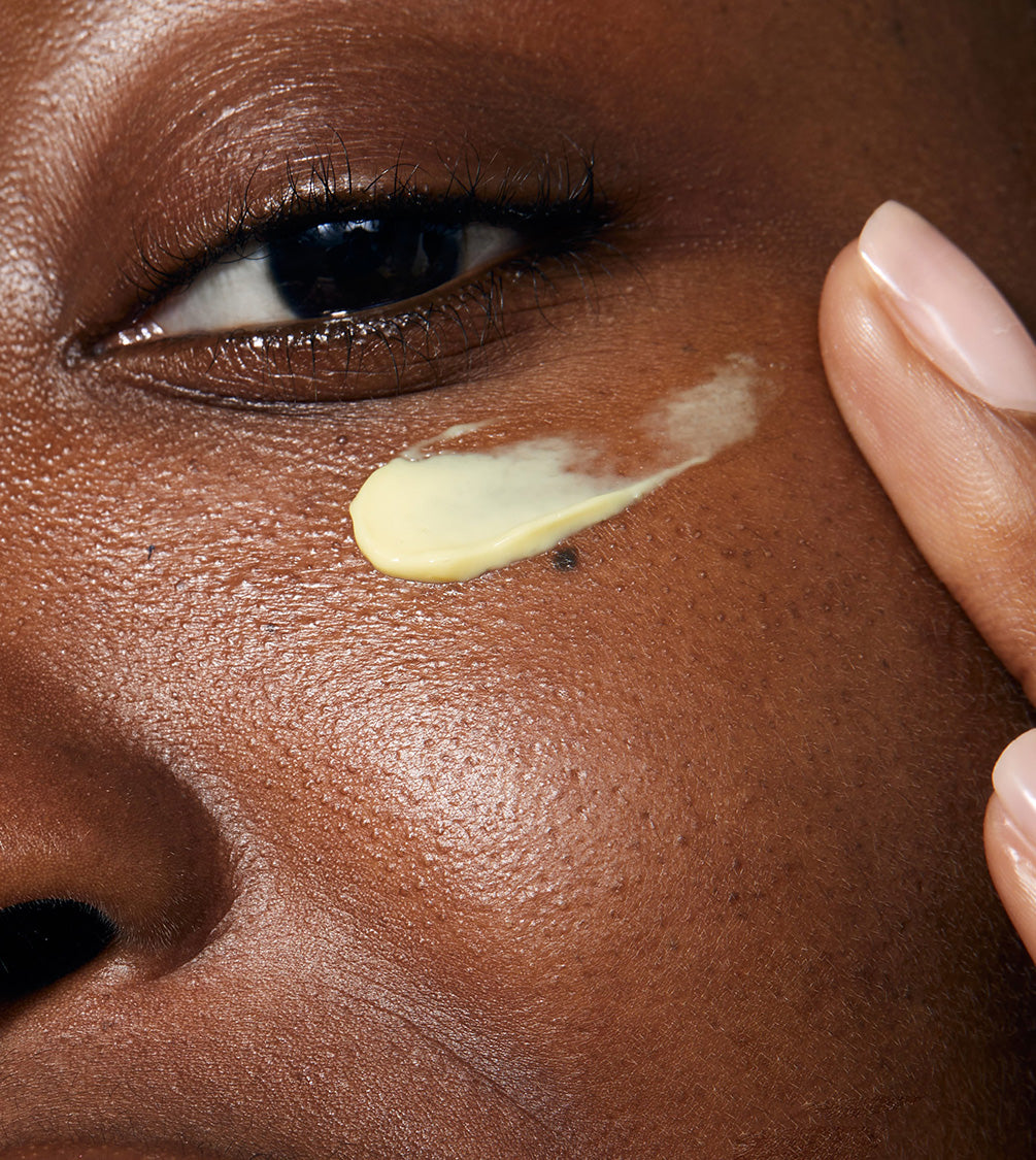 A close up of model's face applying Illumineye Caround her eyes. The product looks rich and hydrating on her skin