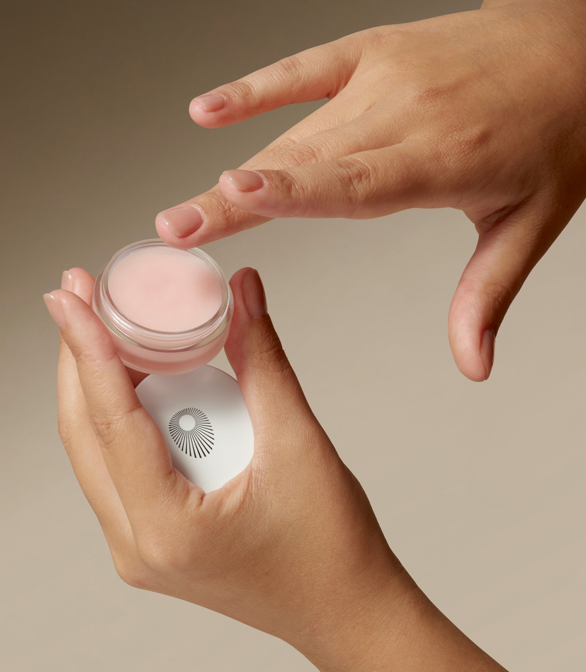 Hands are holding a jar of Perfecting Lip Balm.