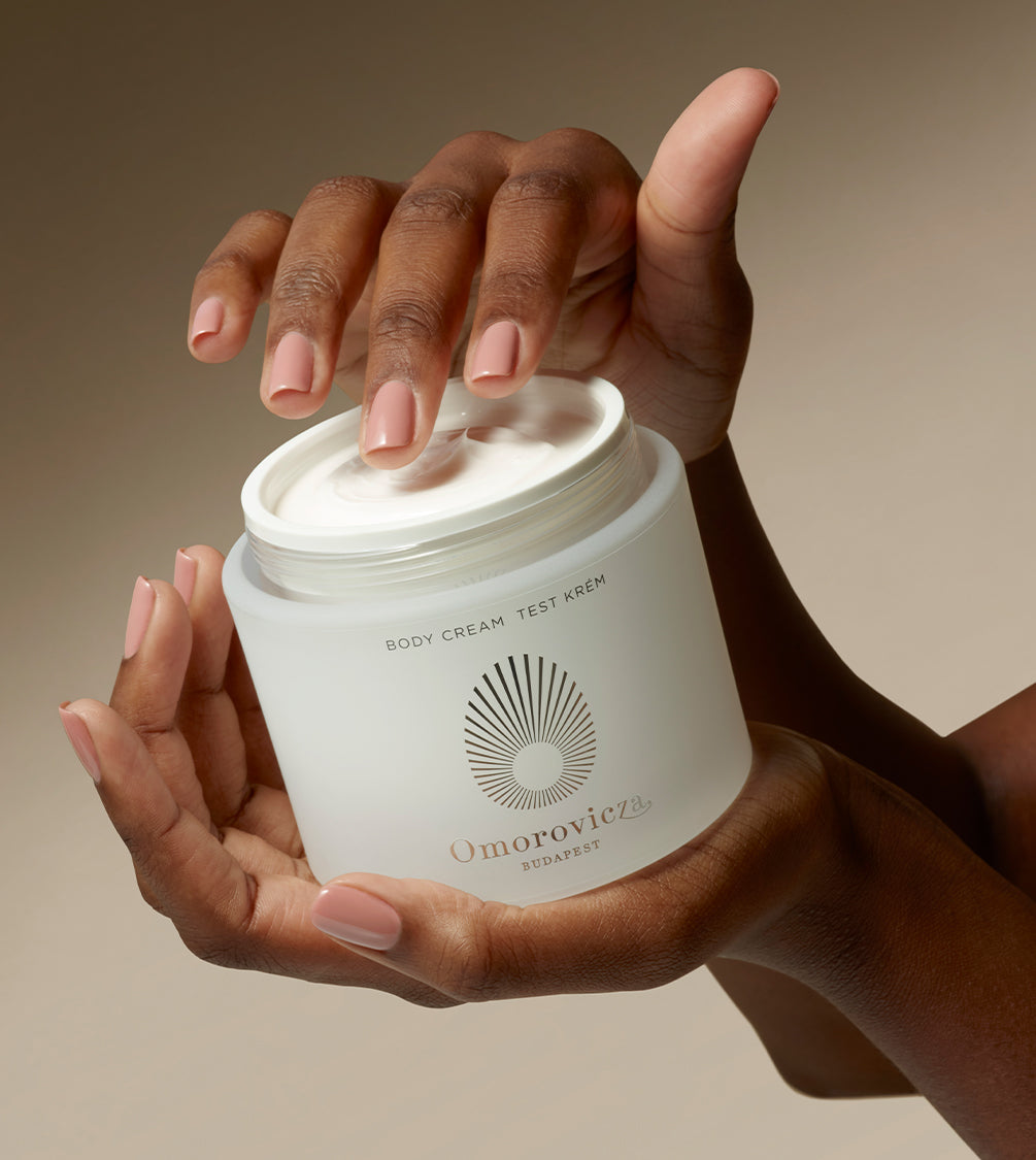 Hands are holding a jar of Omorovicza Body cream.