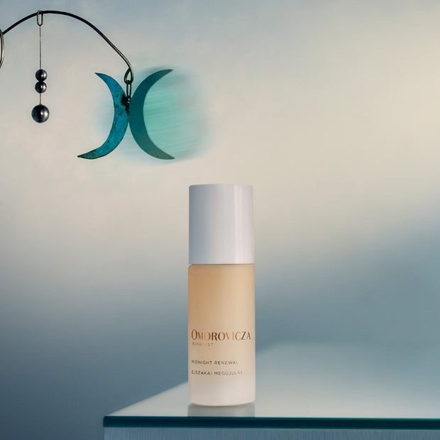 Omorovicza Midnight Renewal bottle on a reflective surface with a decorative wall hanging in the background