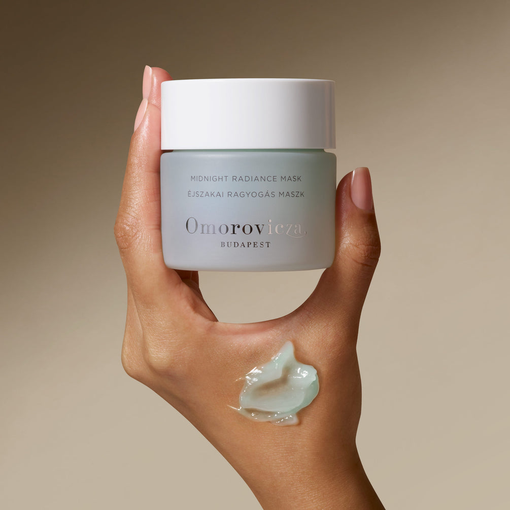 A Hand is holding a jar of Midnight Radiance Mask with a swatch of the product on the skin. 