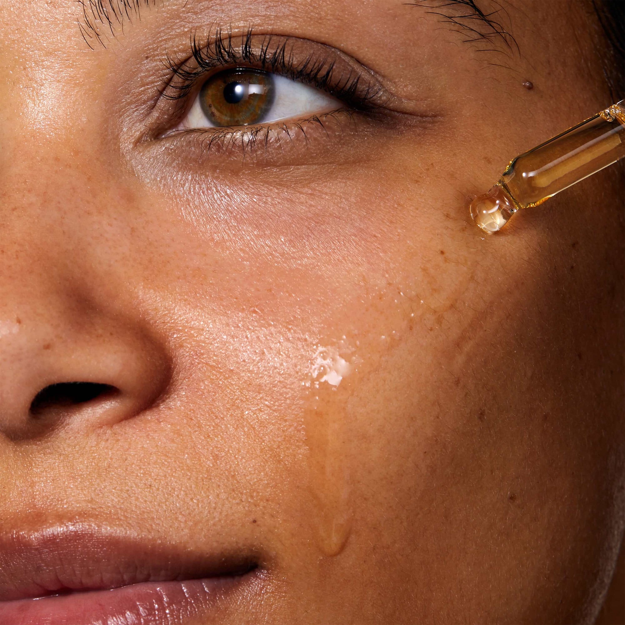 Model applying Miracle Facial Oil to her face with a pipette. The skin where the product has been applied look glowy and hydrated.